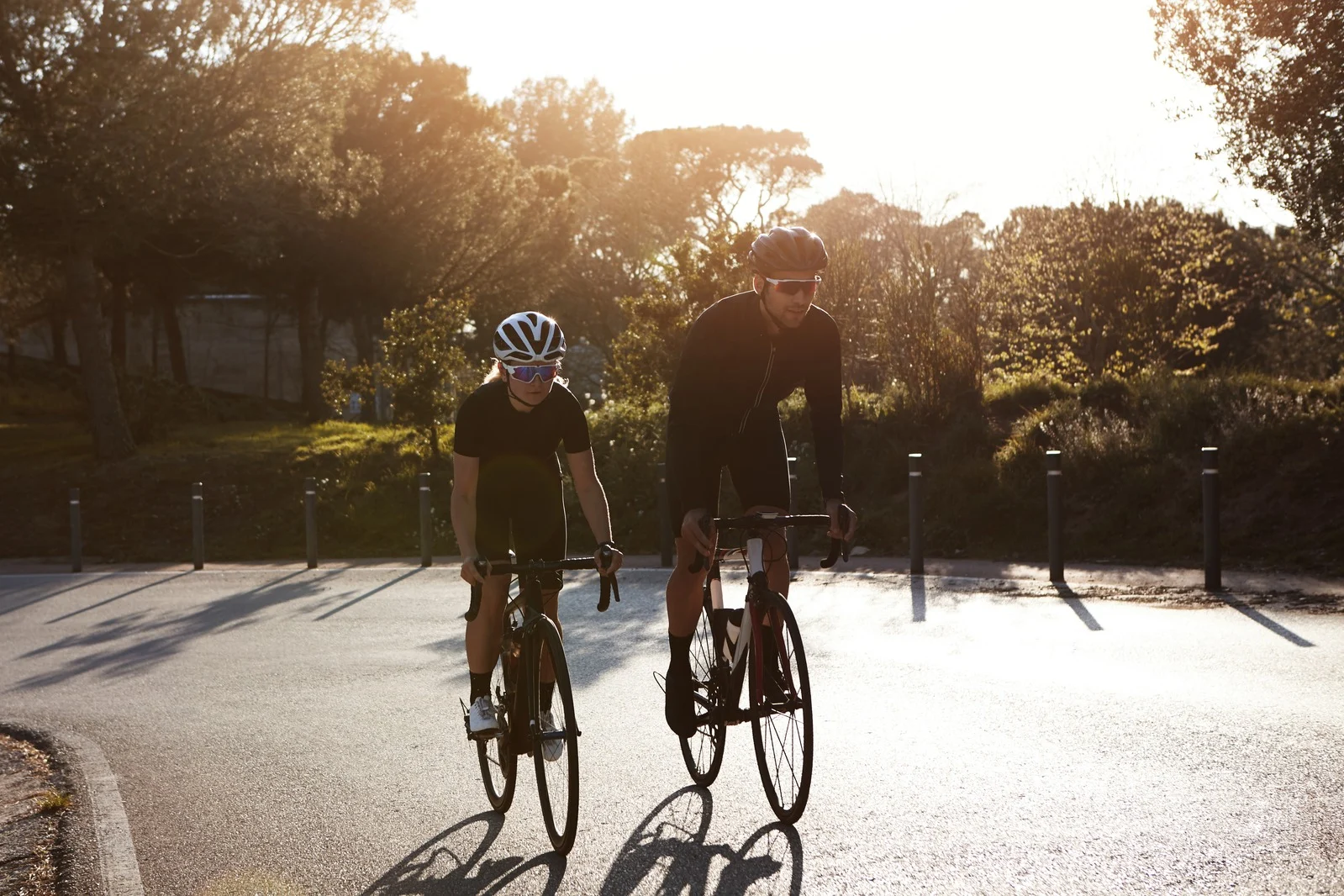 Dois ciclistas a pedalar juntos numa estrada arborizada