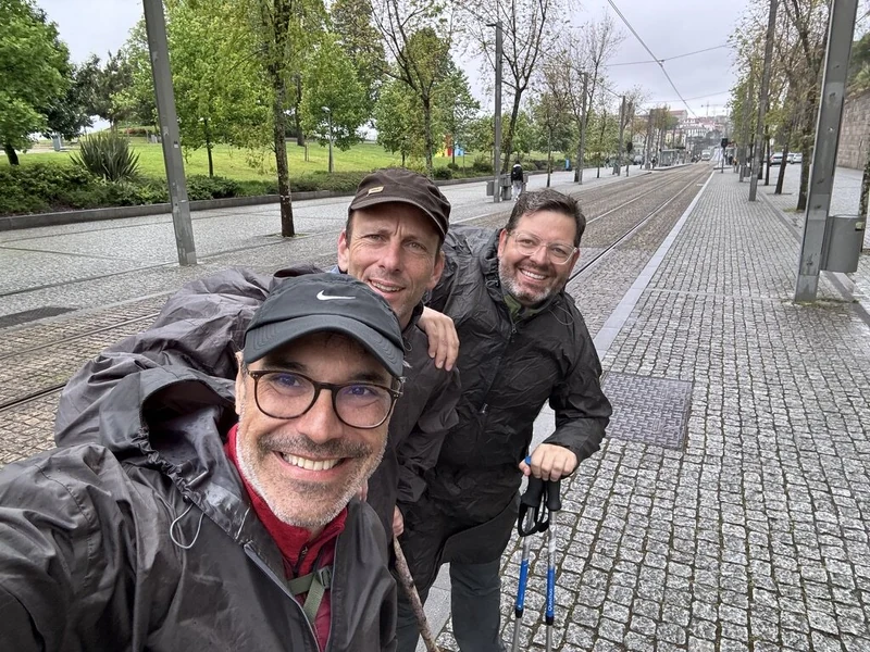 Três homens de mochila caminham juntos numa rua da cidade.